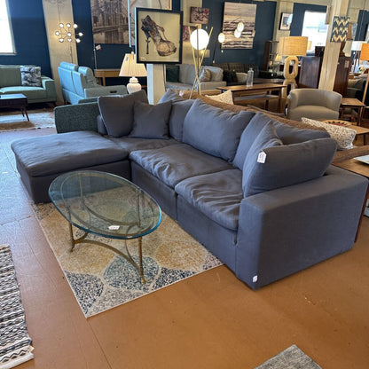 Gray sectional sofa in a showroom with glass coffee table and various decor items.