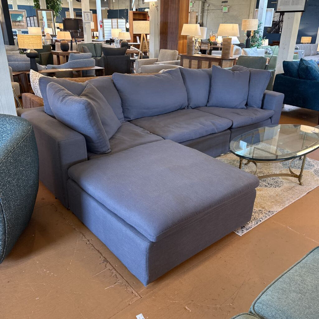 Gray sectional sofa in a showroom setting with other furniture and decor.