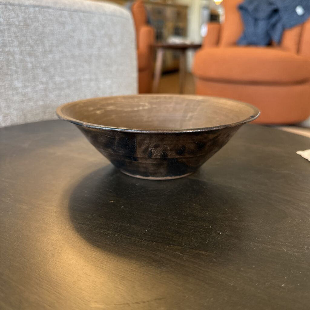Brown ceramic bowl on a dark wooden table with blurred furniture in the background