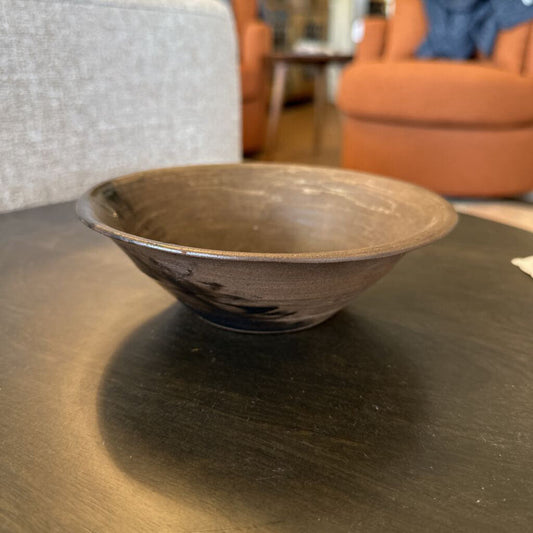 Brown ceramic bowl on a dark surface with blurred indoor background