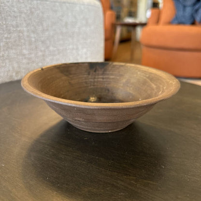 Brown ceramic bowl on a dark surface with blurred indoor background