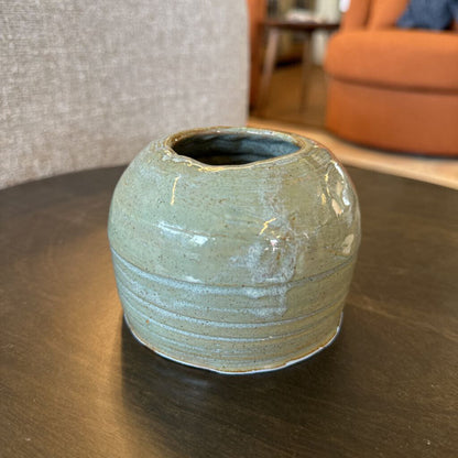 Green ceramic vase on a wooden table with a blurred indoor background