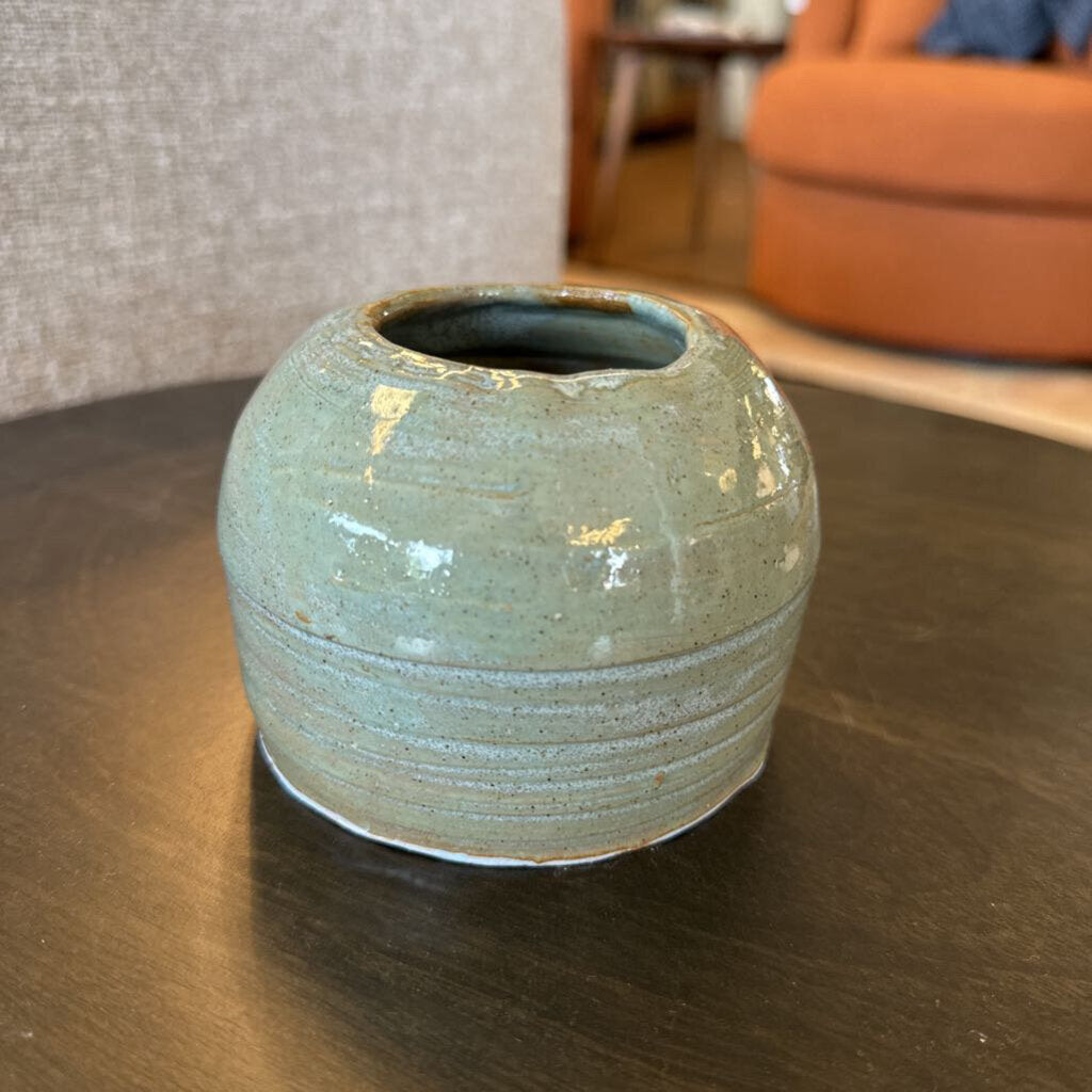 Green ceramic pot on a wooden table with a blurred indoor background