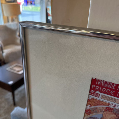 Partial view of a framed picture leaning against a textured wall with a blurred indoor setting.