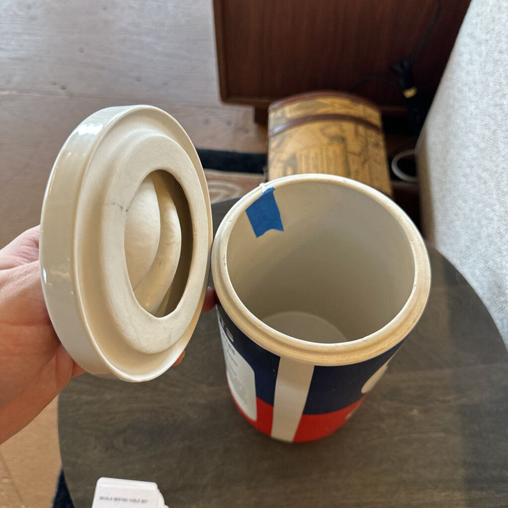 Person holding a cylindrical container with a lid, showing a Union Jack design on a wooden surface.