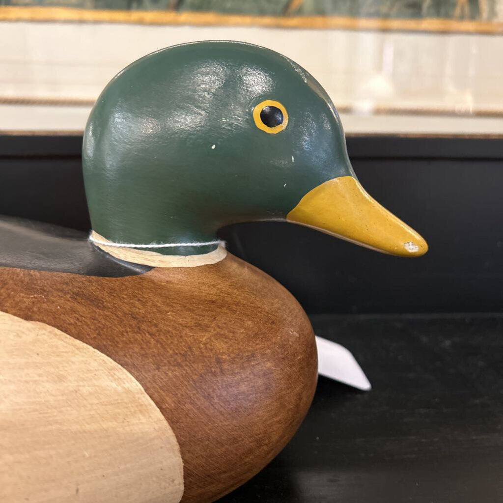 Wooden duck decoy with green head and brown body on a dark surface