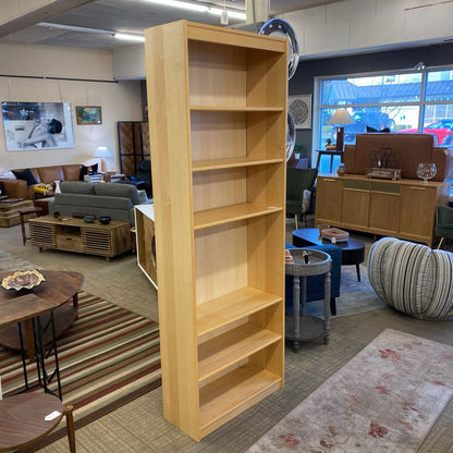 Tall wooden bookshelf in a living room setting with furniture and decor.