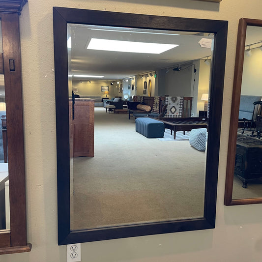 Large mirror with a dark frame reflecting a living room.