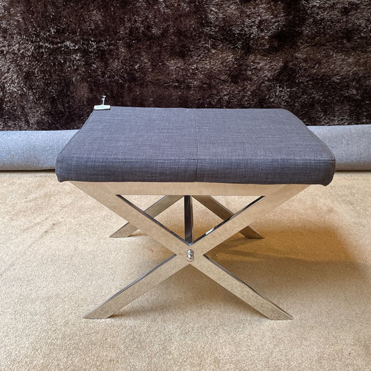 Gray upholstered bench with metal X-shaped legs on a beige carpet