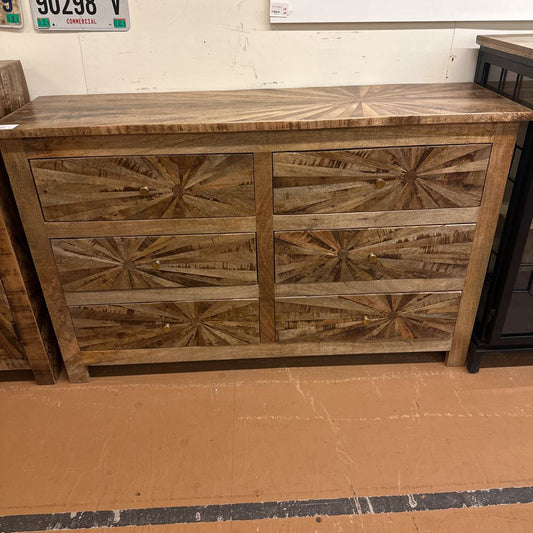 Wooden dresser with starburst pattern on a cardboard floor.