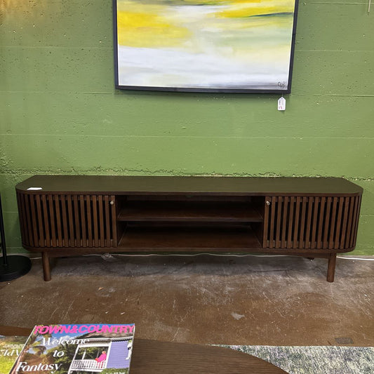Wooden TV stand against a green wall with a magazine on a table in the foreground.