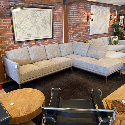 Gray sectional sofa in a room with brick walls, framed maps, and wooden tables.