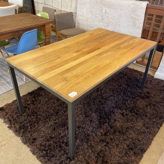 Wooden table with metal legs on a brown rug, surrounded by chairs in a showroom setting.