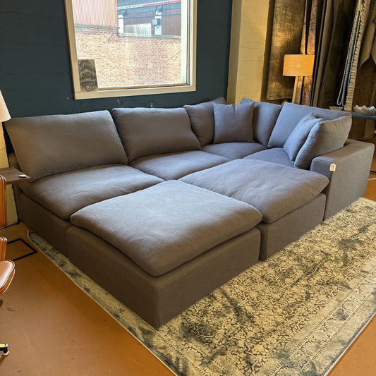 Gray sectional sofa in a living room setting with a rug and lamp.