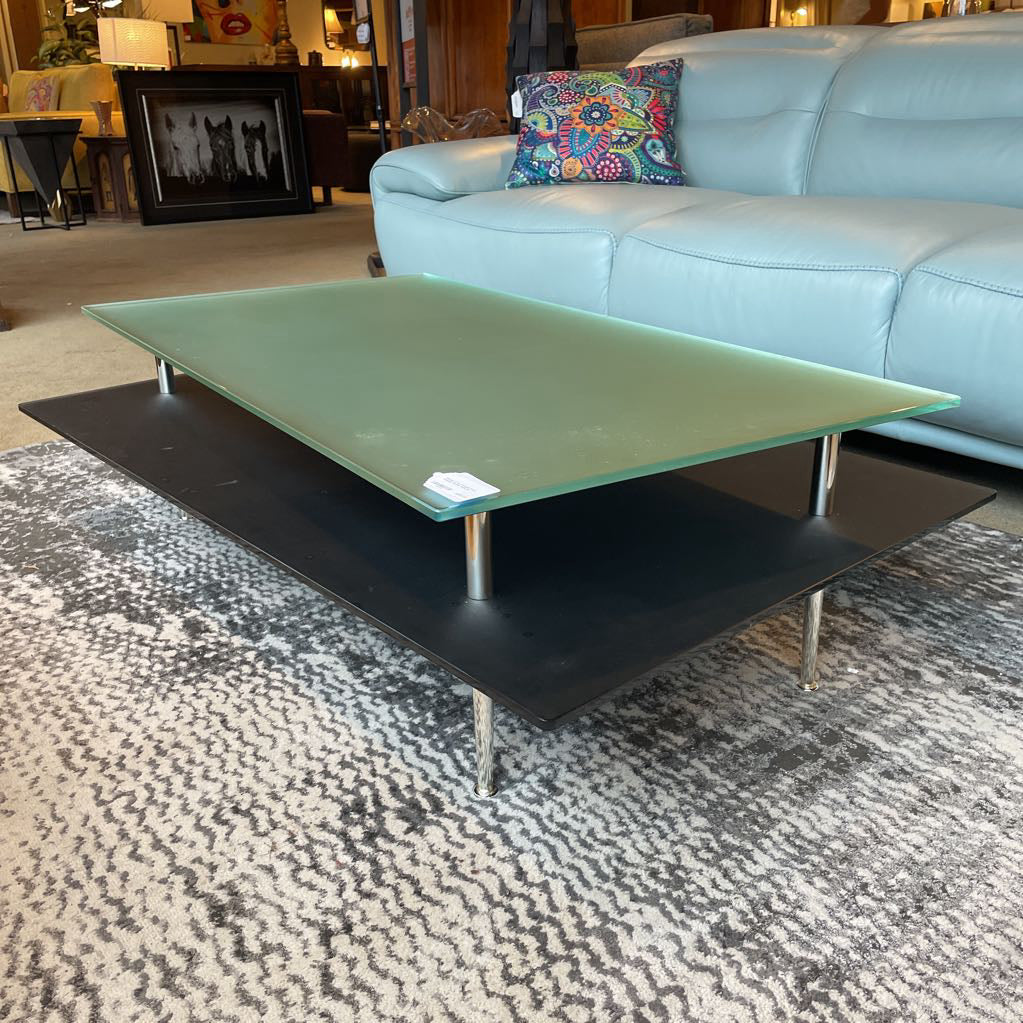Green glass coffee table with black base in a living room setting