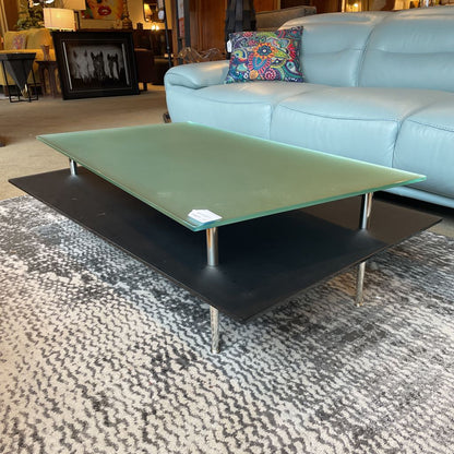 Green glass coffee table with black base in a living room setting