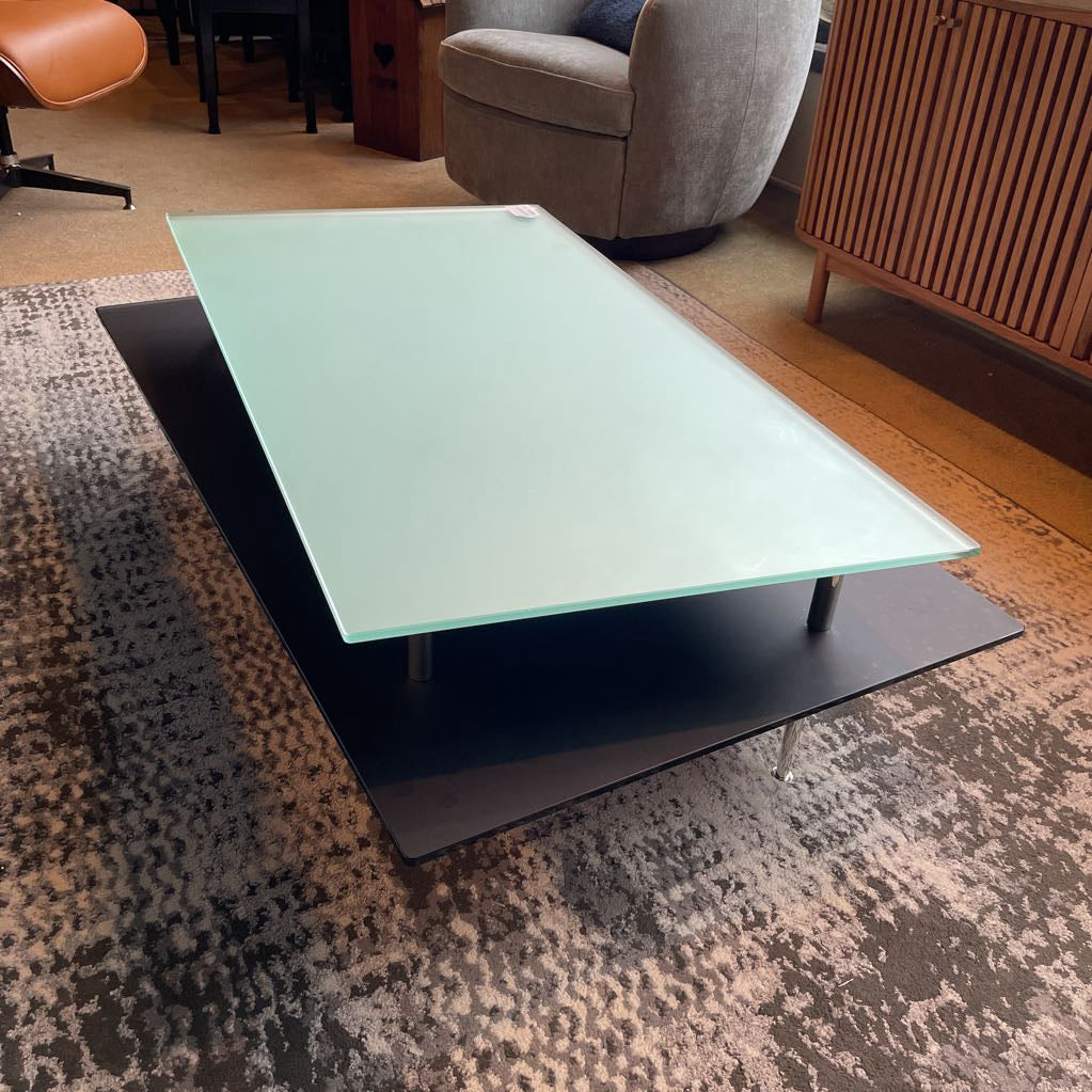 Coffee table with a glass top and black base in a living room setting.