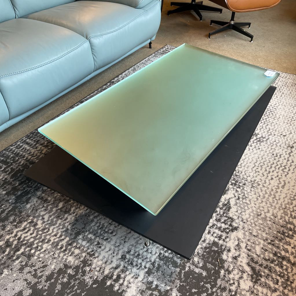 Glass coffee table on a patterned rug with a light blue sofa in the background