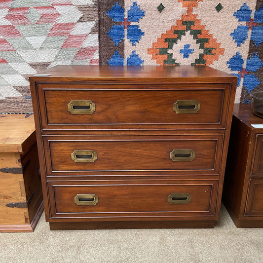 Wooden dresser with brass handles against a patterned rug background
