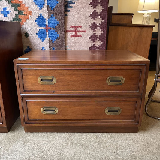 Wooden dresser with two drawers and brass handles in a room setting.