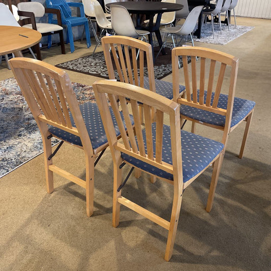 Wooden chairs with blue cushioned seats arranged in a room with carpeted flooring.
