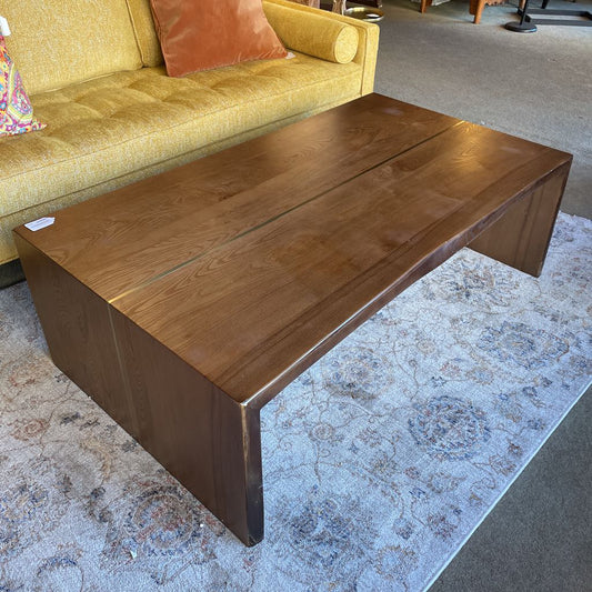 Wooden coffee table in a living room setting with a yellow sofa and patterned rug.