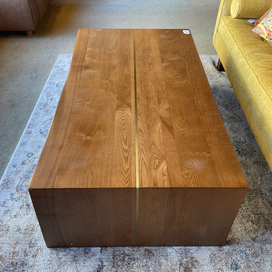 Wooden coffee table in a living room setting with a yellow sofa and gray carpet.