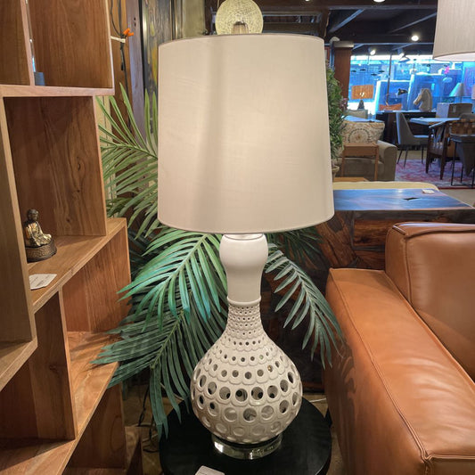 White lamp with beige shade on a table in a room with furniture and decor