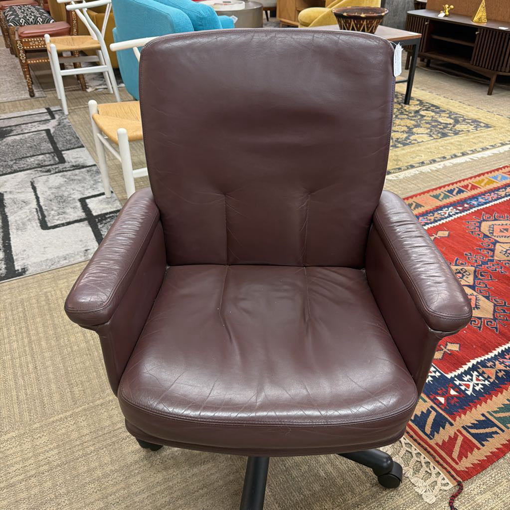 Brown leather office chair in a room with patterned rugs and furniture.