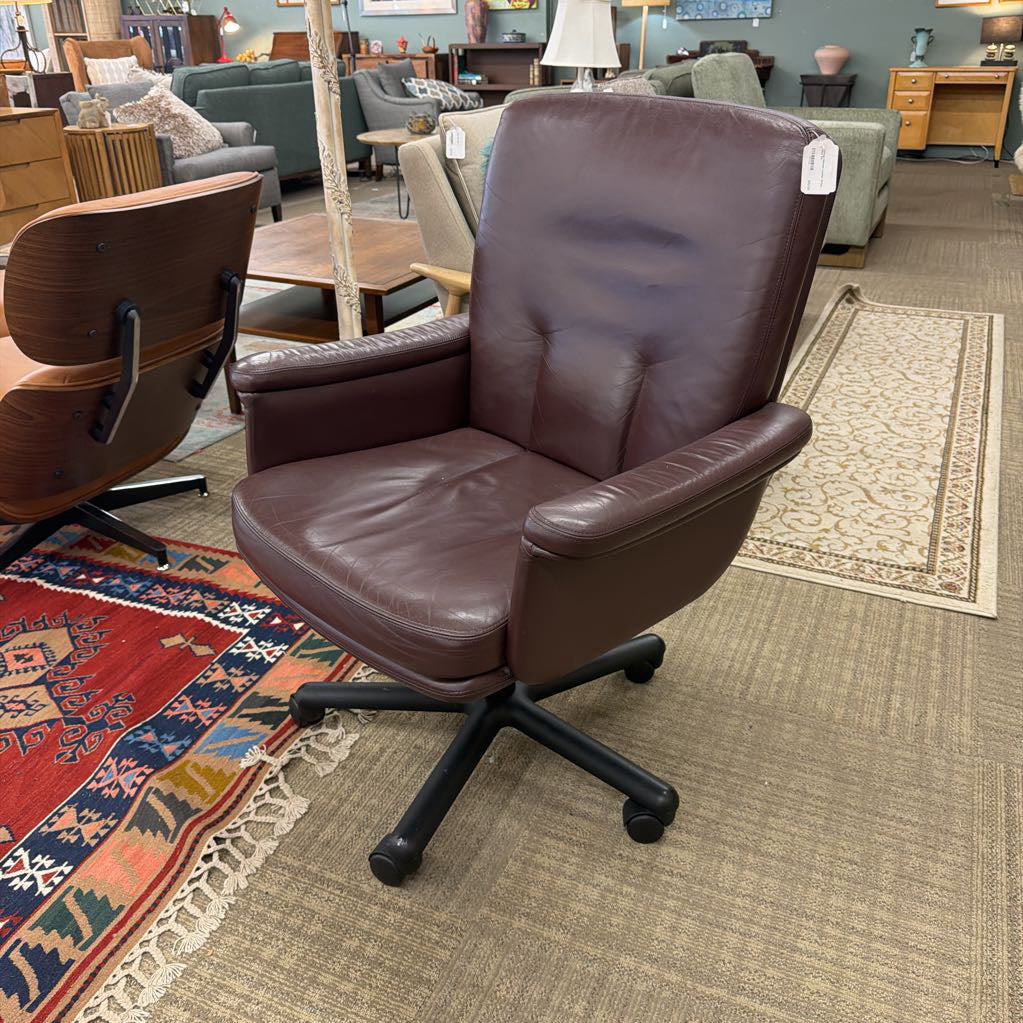 Brown leather office chair in a showroom setting with other furniture.