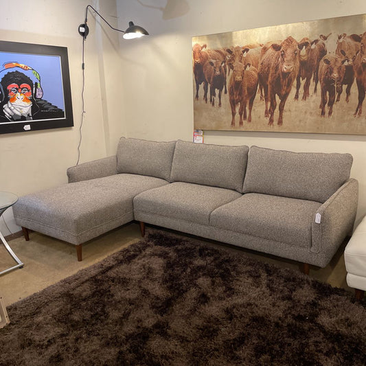 Gray sectional sofa in a living room with a painting of cows on the wall.