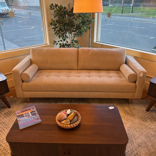 Beige sofa in a room with a wooden coffee table and a plant in the background.