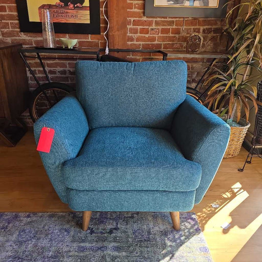 Blue armchair with a red tag in a room with brick walls and a plant.