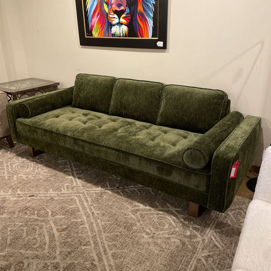 An olive green textured three-seater sofa with a button-tufted seat, three back cushions, and two bolster pillows, resting on a grey patterned rug