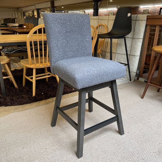 Gray bar stool with black legs in a room with wooden furniture and a rug.