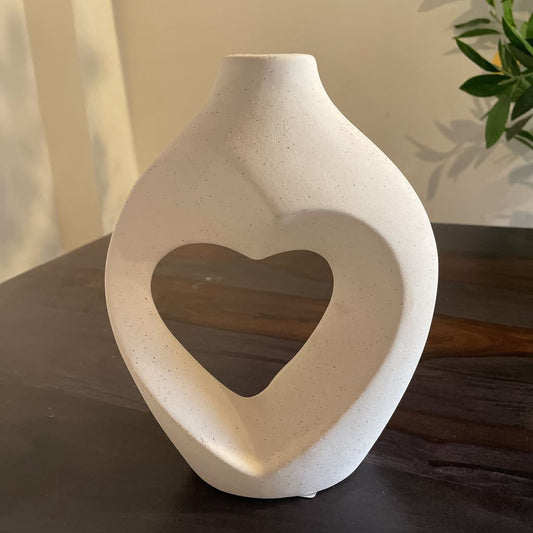 White ceramic vase with a heart-shaped cutout on a wooden surface.
