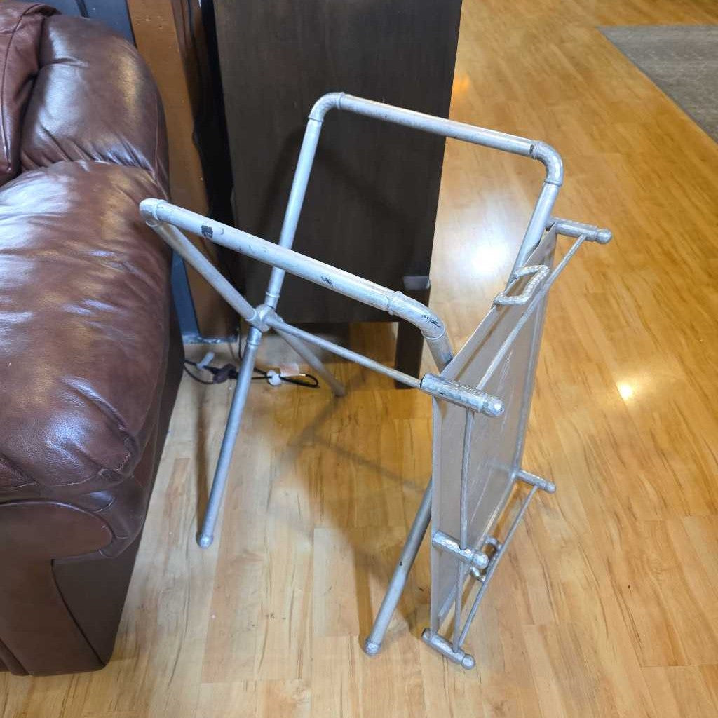 Metal magazine rack on a wooden floor next to a brown leather couch