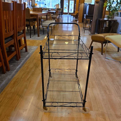 Metal serving cart on a wooden floor with chairs and tables in the background