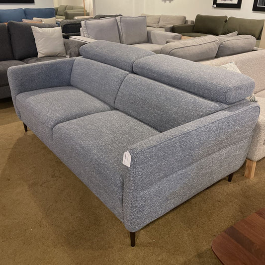 Gray sectional sofa in a showroom setting with other furniture in the background.