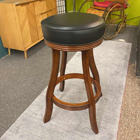Wooden bar stool with black cushioned seat in a room setting.