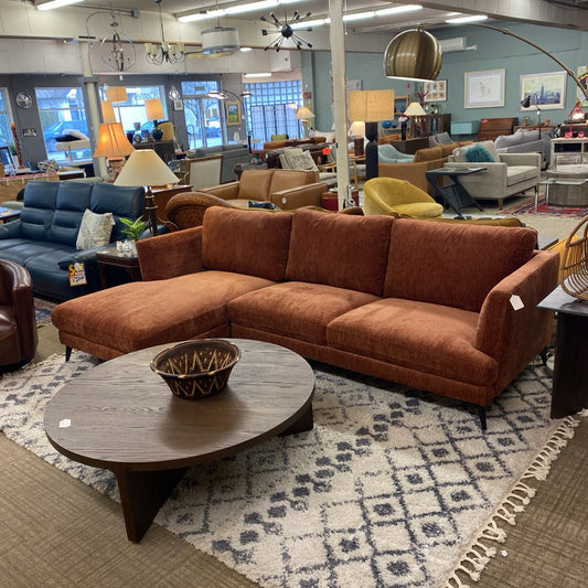 Brown sectional sofa in a showroom with various furniture and decor items.