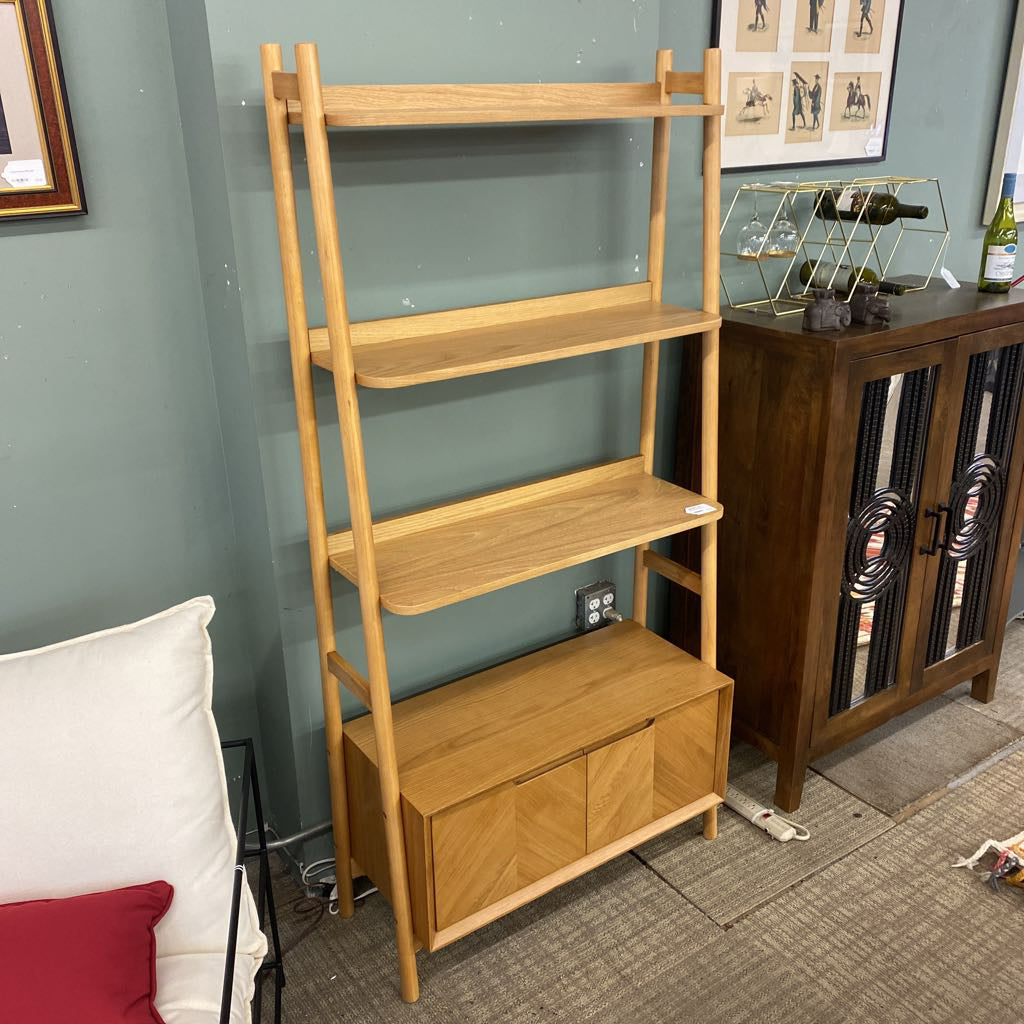 Wooden ladder shelf against a wall with a couch and decorative items in the background.