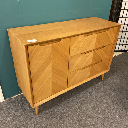 Wooden dresser with two doors and three drawers against a teal wall.