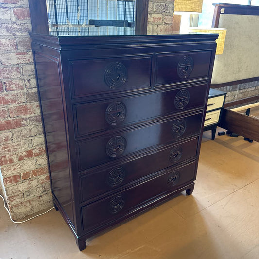 Dark wood dresser with decorative knobs against a brick wall.