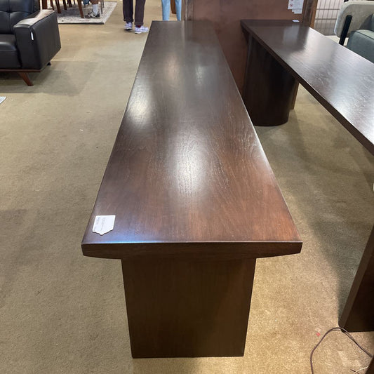 Long dark brown wooden table in a room with carpeted floor and furniture.