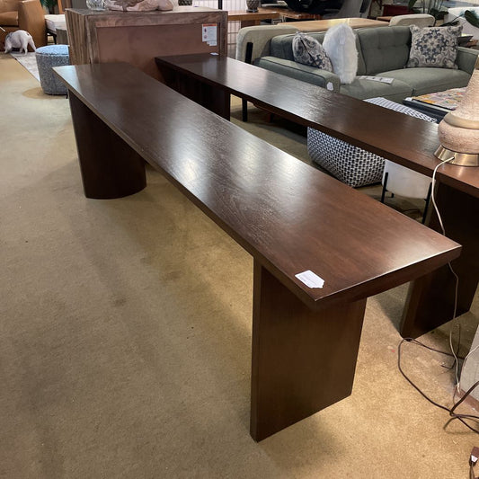 Long dark brown wooden table in a showroom setting with furniture in the background.