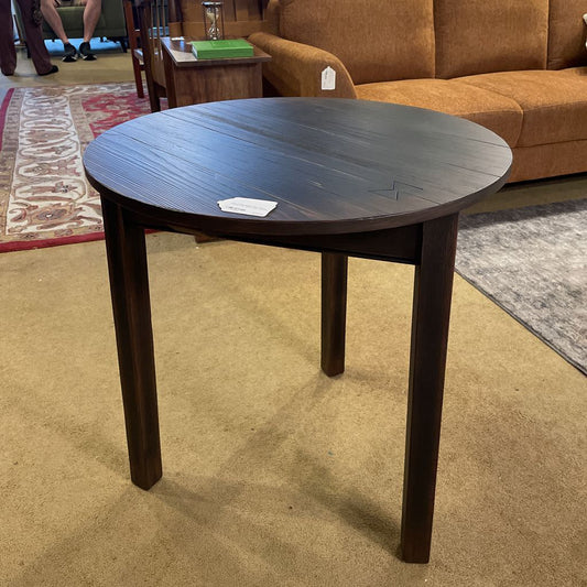 Round dark wood table in a room with a brown couch and patterned rug.