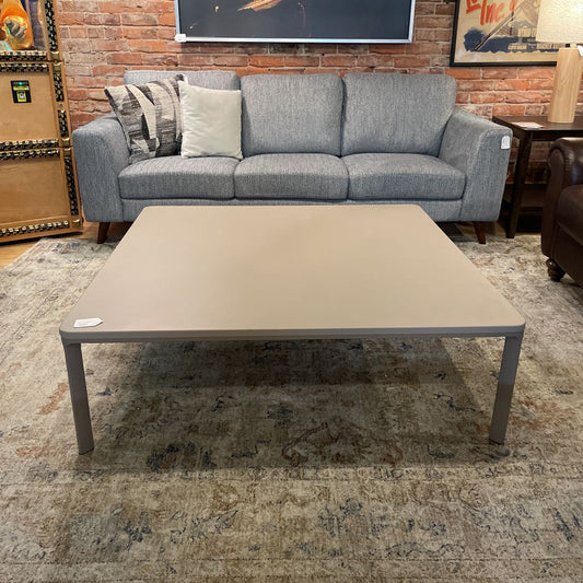 Beige coffee table in front of a gray sofa with decorative pillows in a room setting.