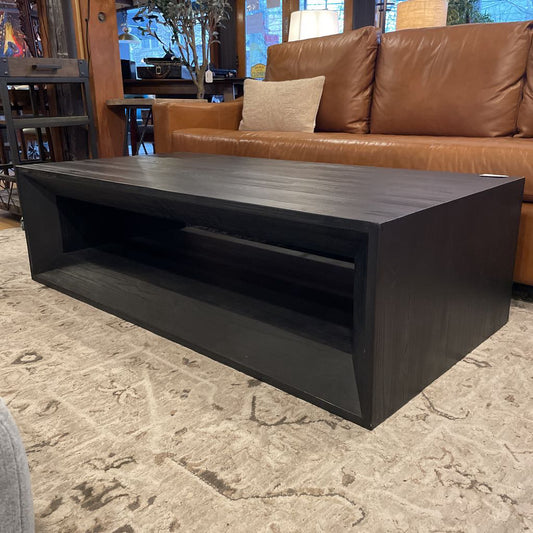 Dark wooden coffee table in front of a brown leather sofa with a patterned rug underneath.