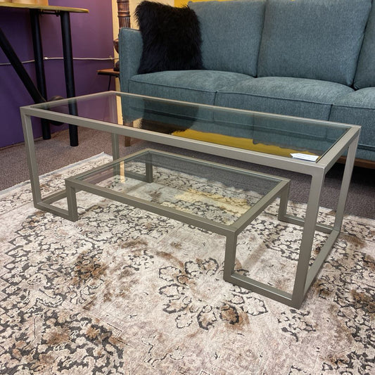 Glass coffee table with metal frame on a patterned rug in a living room setting.